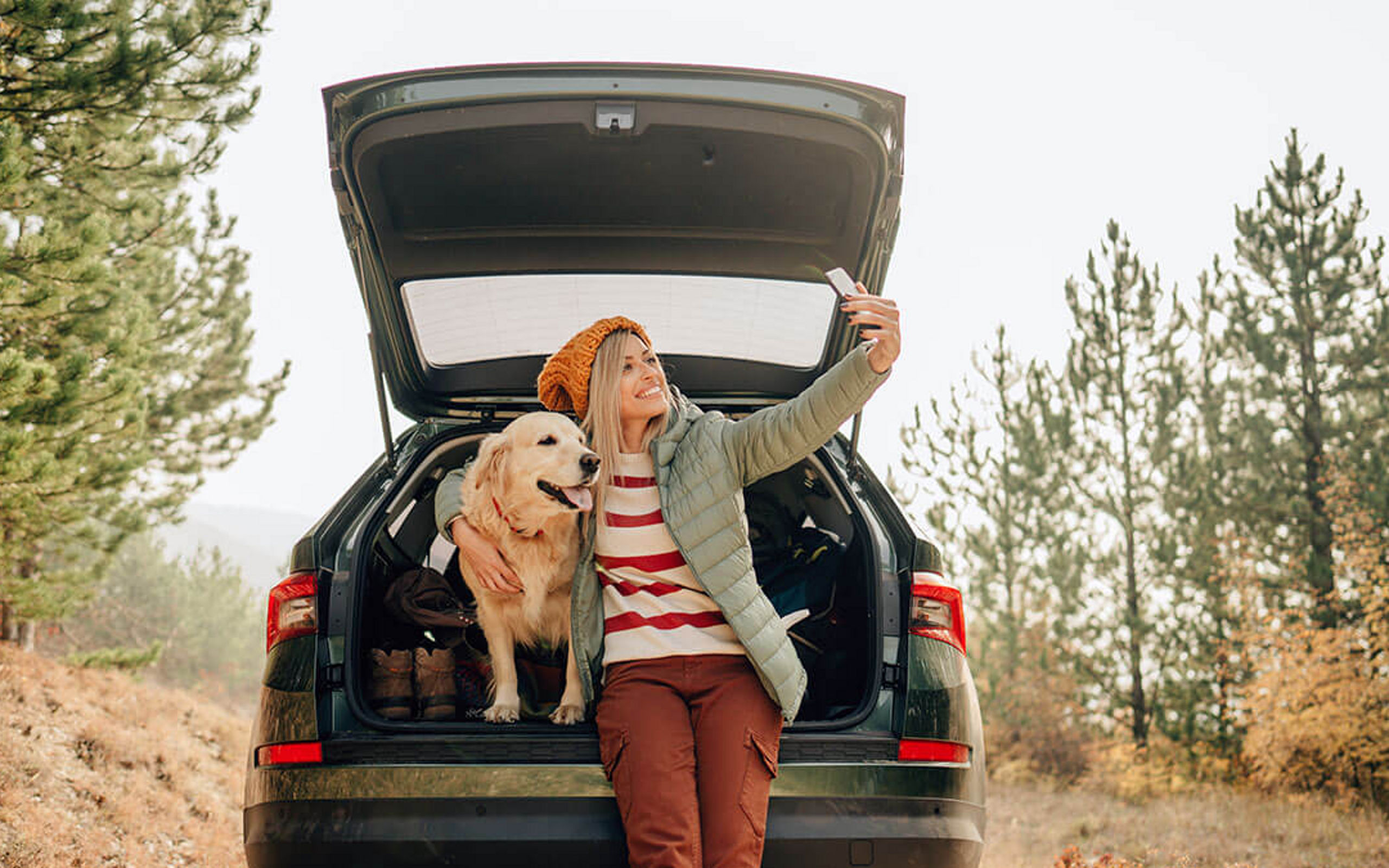 Eine Frau macht mit Ihrem Hund ein Selfie im Kofferaum