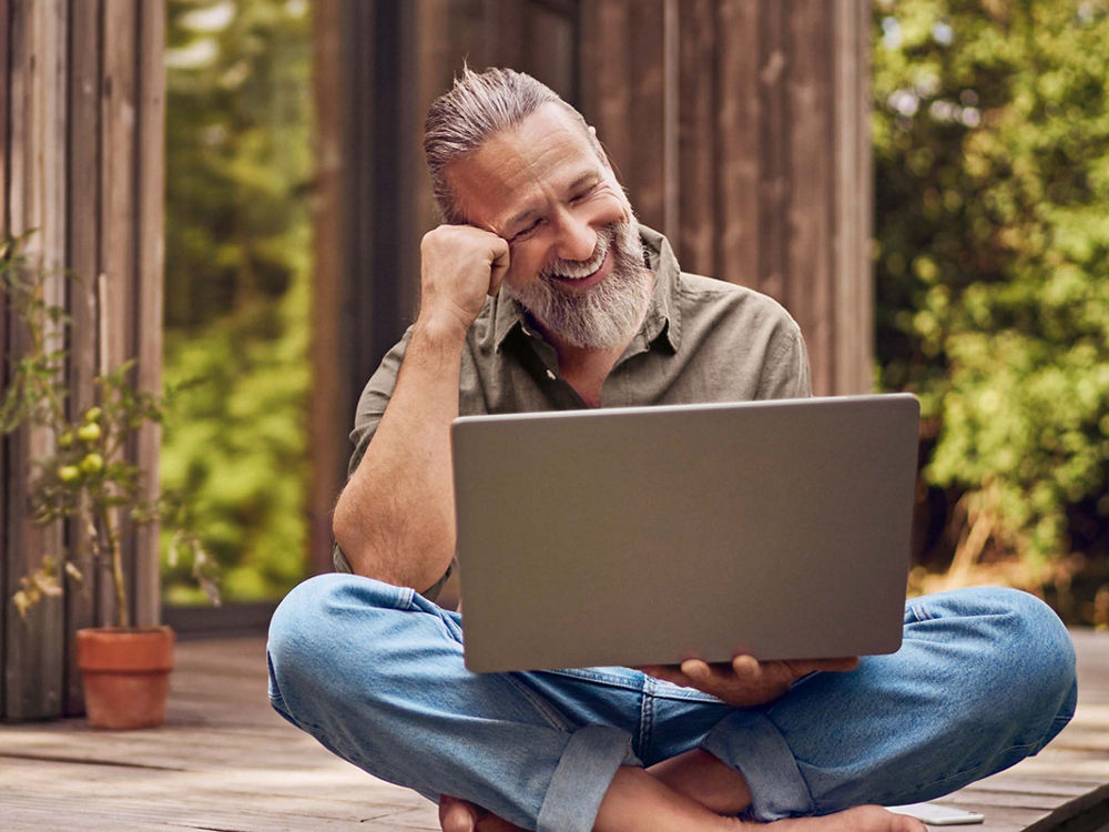 Ein Mann sitzt mit einem Laptop im Freien auf einem hölzernen Podest