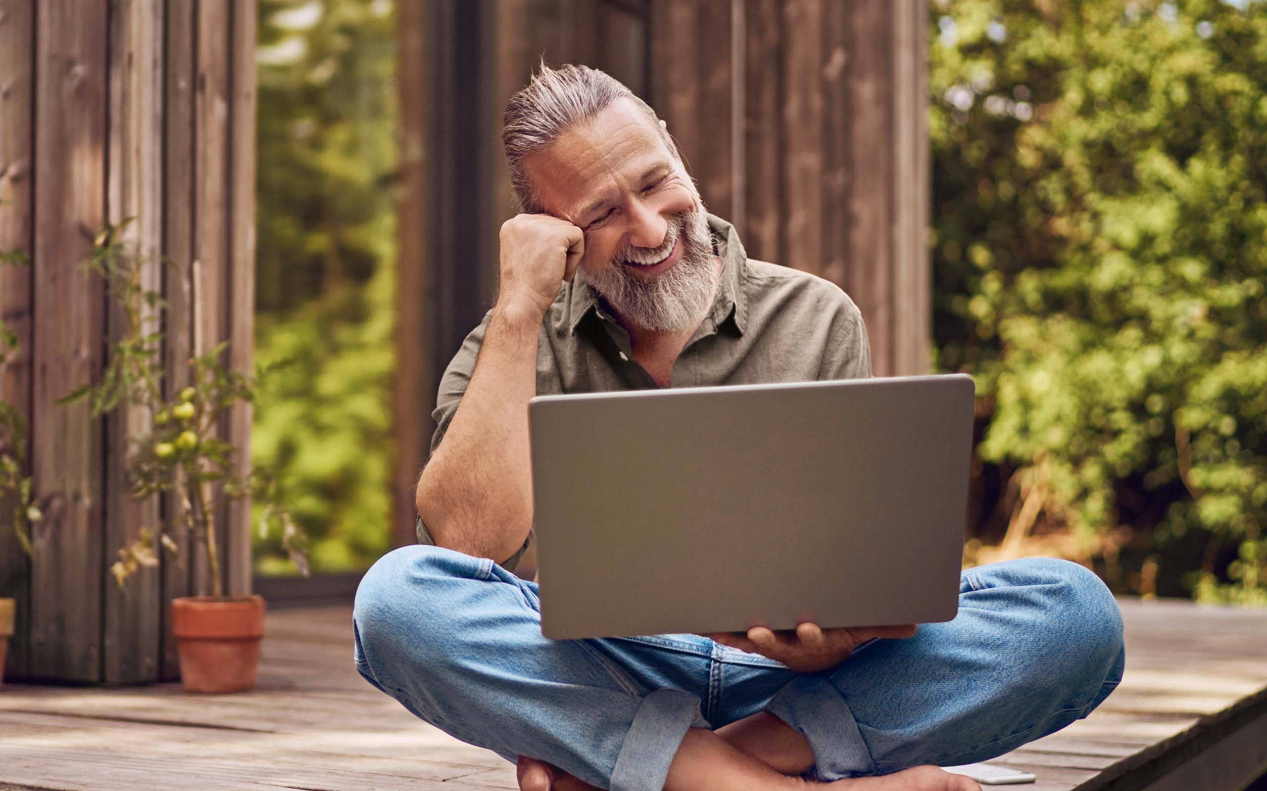 Ein Mann sitzt mit einem Laptop im Freien auf einem hölzernen Podest