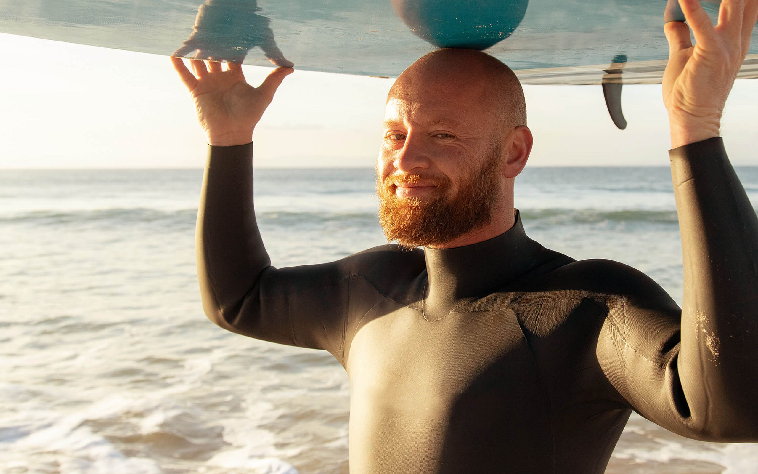 Ein Mann am Strand trägt ein Surfbrett auf dem Kopf