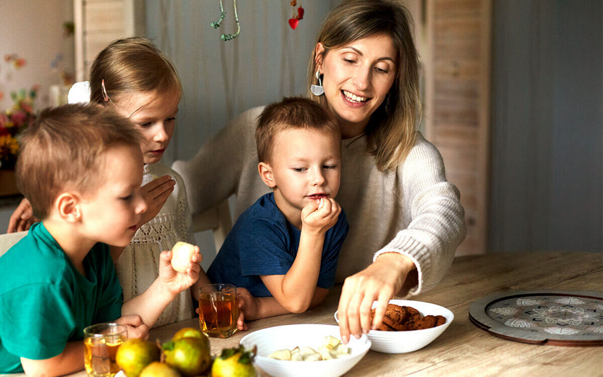 Eine junge Frai mit drei Kindern, die Obst und Kekse naschen