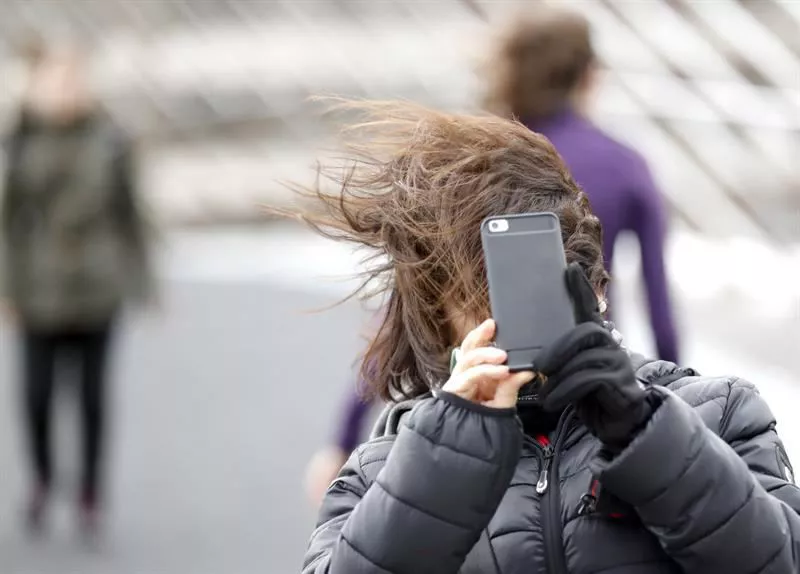 Una mujer hace frente al viento al tratar de sacar una foto. Foto: EFE