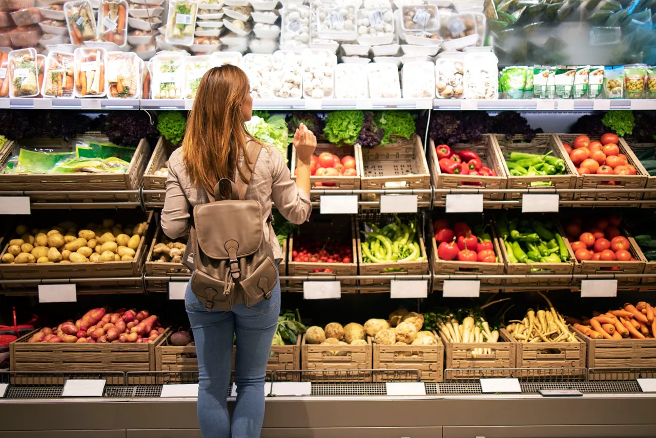 Good looking woman standing in front of vegetable shelves choosing what to buy.