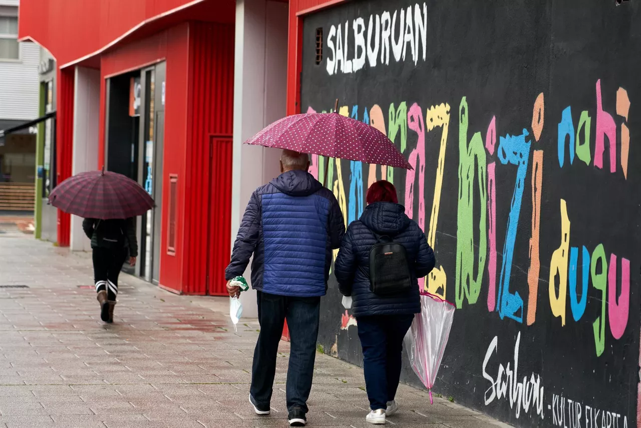 Varias personas en el barrio de Salburua en Vitoria-Gasteiz se protegen de la lluvia.