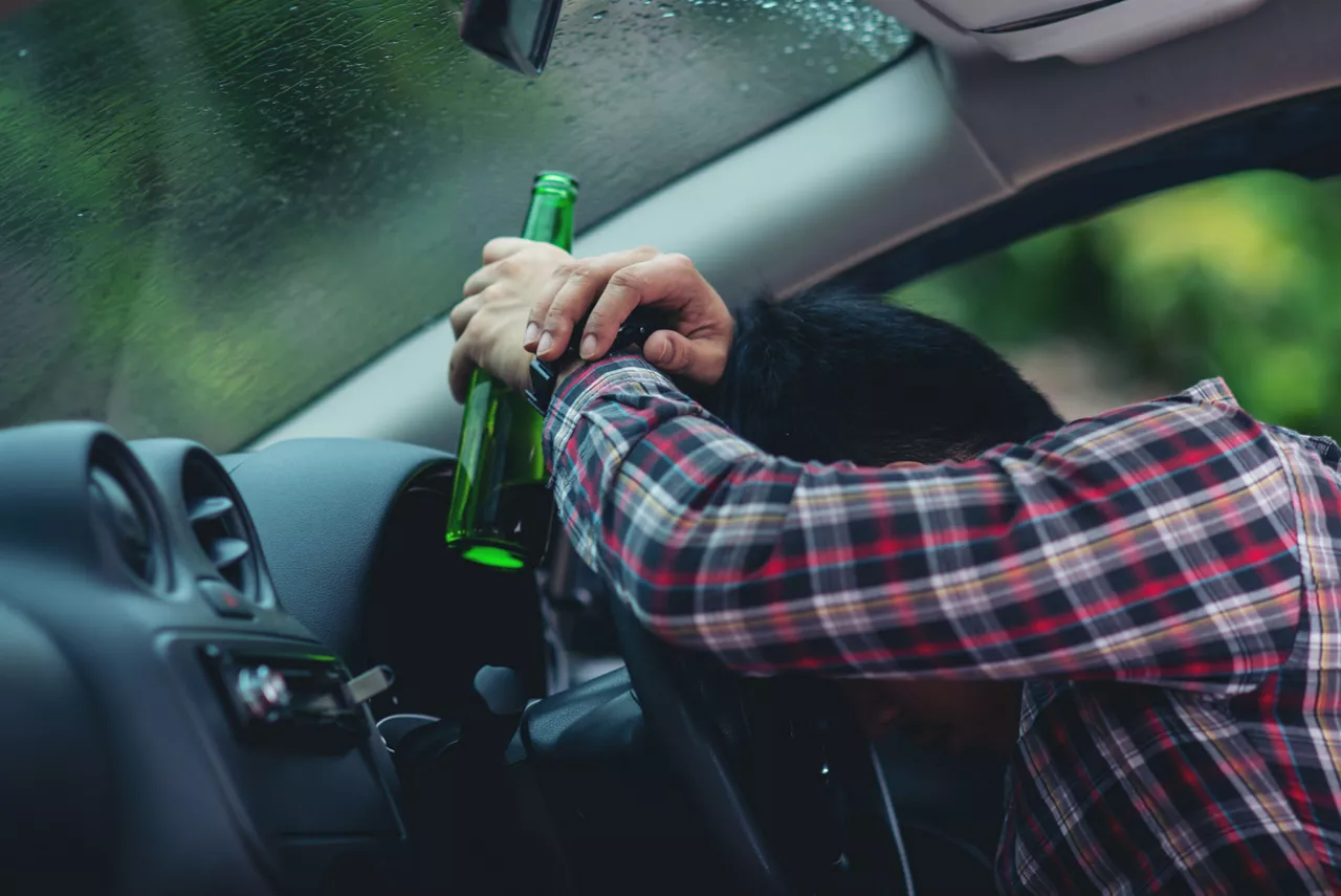 Hansome man holding beer bottle while driving a car