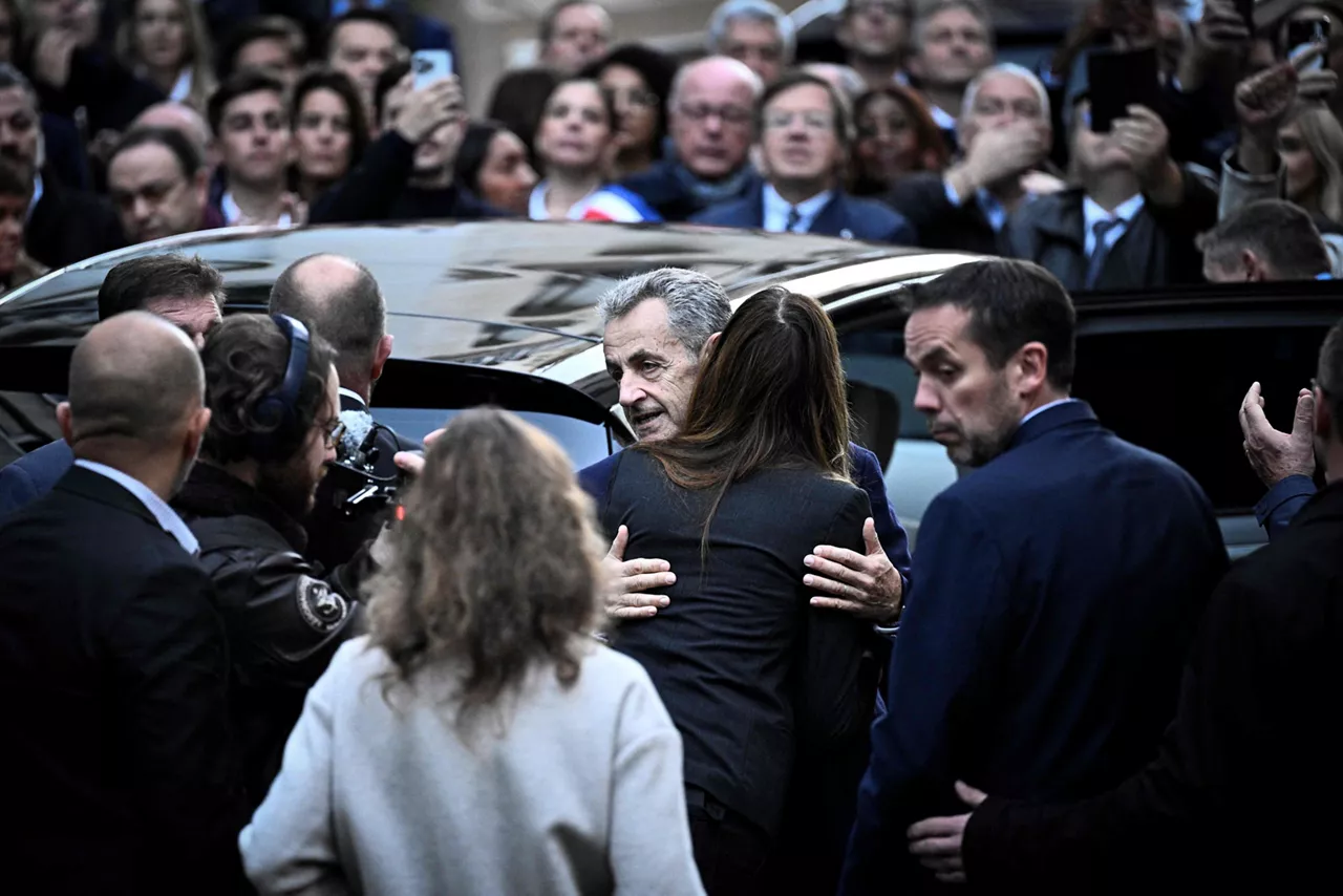 21 October 2025, France, Paris: France's former president Nicolas Sarkozy (C) hugs his wife Carla Bruni-Sarkozy as he leaves his residence to present himself to La Sante Prison for incarceration on a five-year prison sentence after being convicted of criminal conspiracy over a plan for late Libyan dictator Moamer Kadhafi to fund his 2007 electoral campaign. Former French president Nicolas Sarkozy is set to begin his prison sentence in La Santé prison in central Paris on Tuesday, after being sentenced to five years in connection with illegal campaign funding from Libya. Photo: Julien De Rosa/AFP/dpa