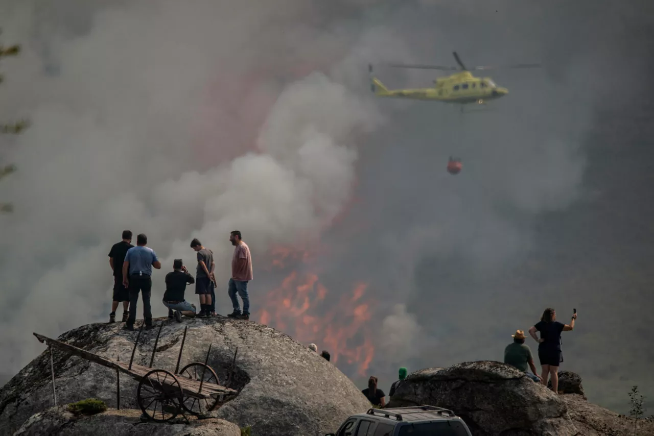 AVIÓN (OURENSE), 25/08/2025.- Varias personas observan la labor de un helicóptero de extinción del incendio forestal declarado ayer en Avión (Ourense), este lunes. EFE/Brais Lorenzo
