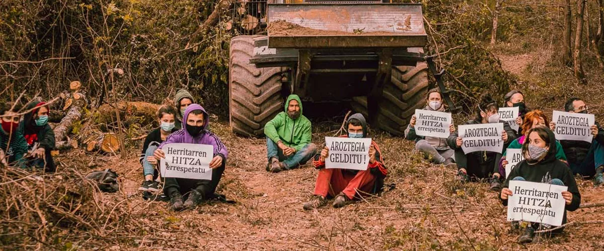 Jóvenes sentados con carteles frente a una excavadora. Foto. Eguzki.
