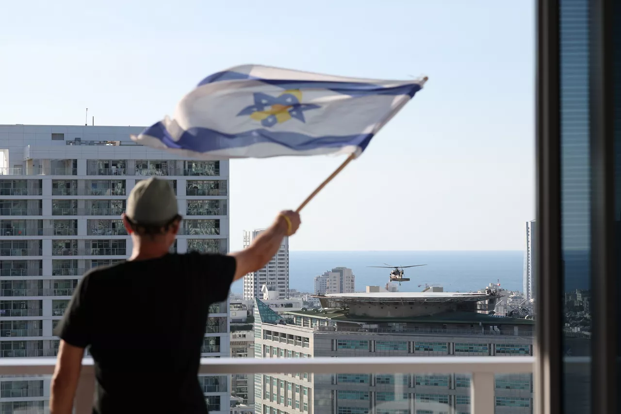 TEL AVIV (Israel), 13/10/2025.- A man aves an Israeli flag from a balcony as he arrives a helicopter approaches the helipad of the Ichilov Hospital in Tel Aviv, Israel, 13 October 2025. The first phase of the Gaza peace agreement, reached between Israel and Hamas, includes the release of Israeli hostages and Palestinian prisoners, a partial withdrawal of Israeli forces, and the delivery of humanitarian aid to Gaza. EFE/EPA/ABIR SULTAN
