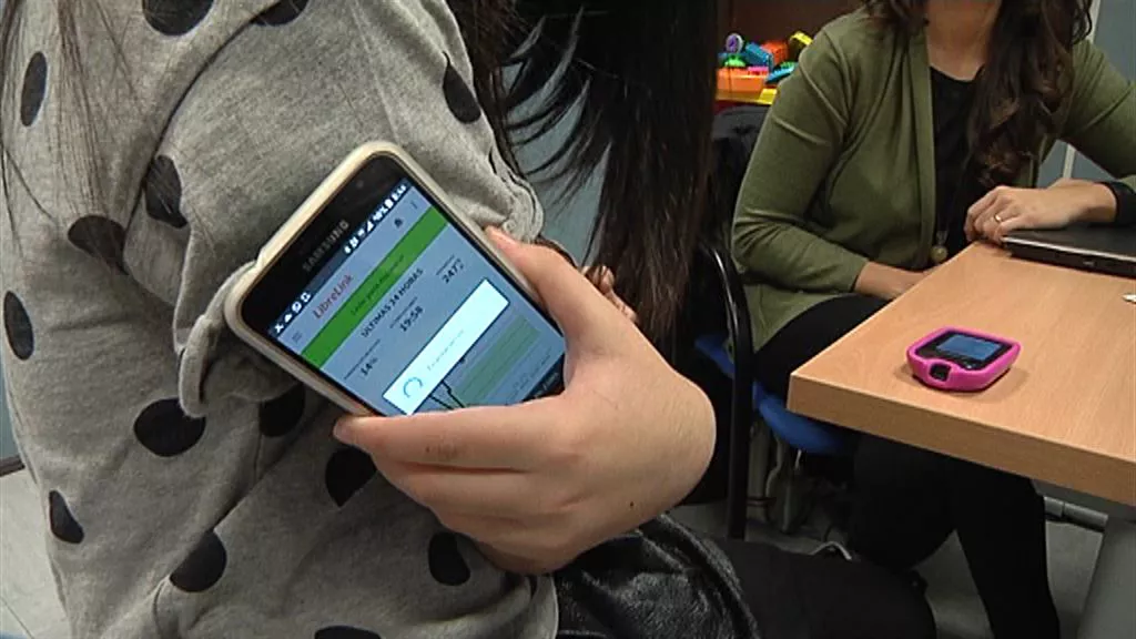 Emakume bat sakelako telefono baten pantailan gluzemia indizea neurtzen.