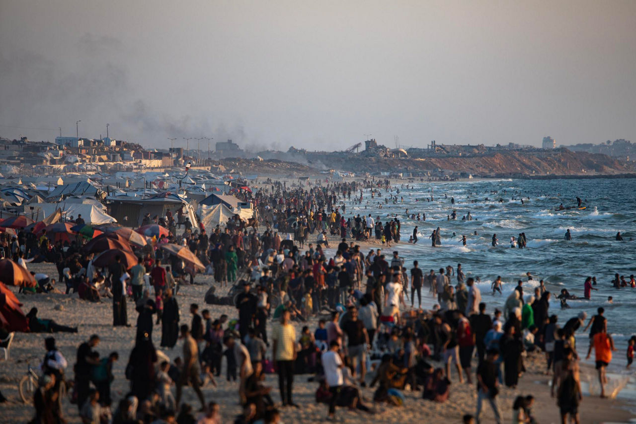 GAZA (-), 20/06/2025.- Smoke rises in the background as internally displaced Palestinians gather on a beach at sunset in Gaza City, 20 June 2025. More than 55,700 Palestinians have been killed in the Gaza Strip, according to the Palestinian Ministry of Health, since Israel launched a military campaign in the strip in response to a cross-border attack led by the Palestinian militant group Hamas on 07 October 2023. EFE/EPA/HAITHAM IMAD
