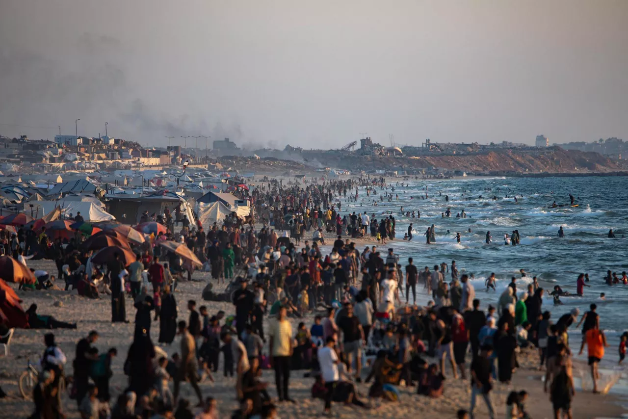 GAZA (-), 20/06/2025.- Smoke rises in the background as internally displaced Palestinians gather on a beach at sunset in Gaza City, 20 June 2025. More than 55,700 Palestinians have been killed in the Gaza Strip, according to the Palestinian Ministry of Health, since Israel launched a military campaign in the strip in response to a cross-border attack led by the Palestinian militant group Hamas on 07 October 2023. EFE/EPA/HAITHAM IMAD
