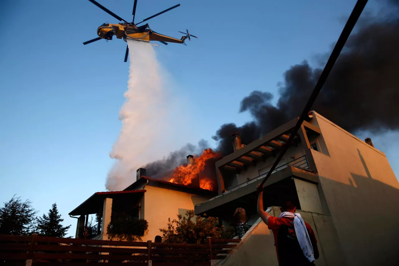 ATHENS (Greece), 26/07/2025.- A firefighting helicopter and volunteers battle to put out a fire burning houses in the residential area of Kryoneri, in the suburbs of Athens, Greece, 26 July 2025. Firefighting forces are battling the wildfire that broke out in Kryoneri, Attica. According to the Fire Service, the fire is considered difficult as it is spreading through a mixed area of forest and residential zones. There are reports of damage to homes, and some have been engulfed in flames. (incendio forestal, Grecia, Atenas) EFE/EPA/YANNIS KOLESIDIS
