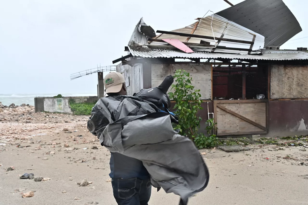 USA5793. PORTMORE (JAMAICA), 27/10/2025.- Un hombre carga una lona para cubrir el techo de una casa antes del paso del huracán Melissa este lunes, en la playa pesquera de Hellshire, en Portmore (Jamaica). El primer ministro de Jamaica, Andrew Holness, aseguró que el Gobierno cuenta con un plan multifacético para llevar a cabo una respuesta "rápida y eficaz" ante el inminente impacto la noche de este lunes del huracán Melissa en el país caribeño. EFE/Rudolph Brown
