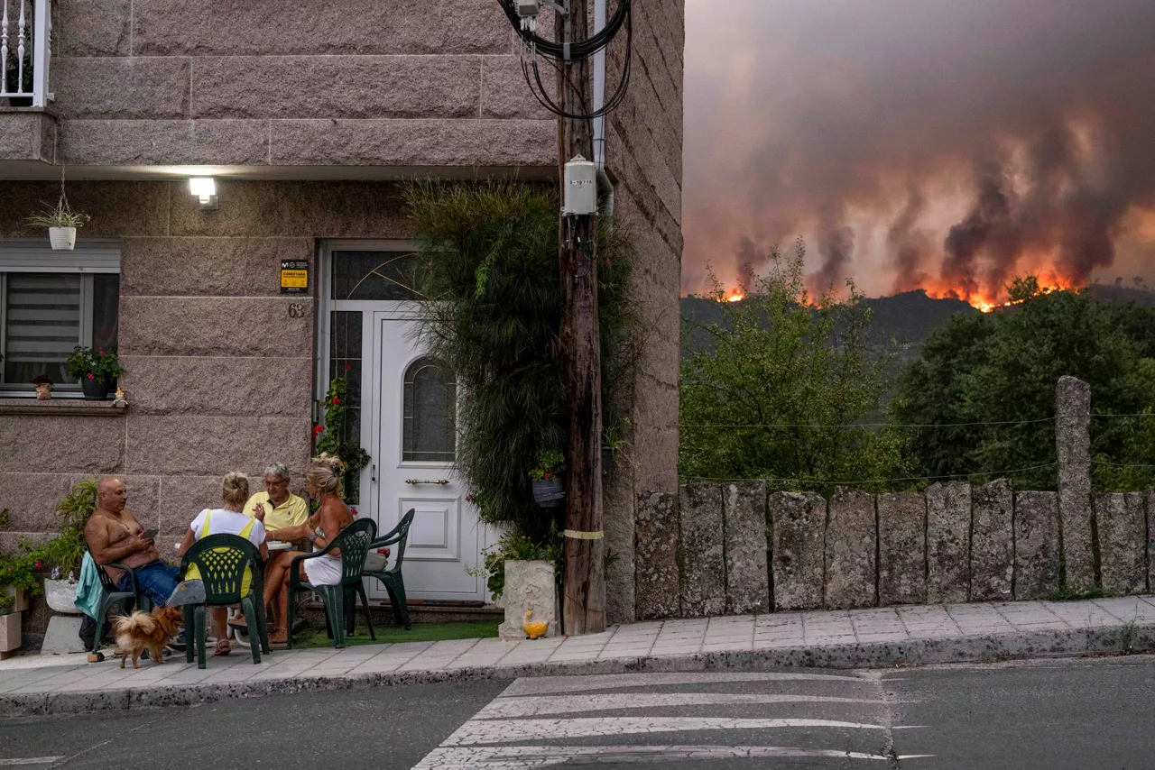 CARBALLEDA DE AVIA (OURENSE), 16/08/2025.- Un grupo de personas juegan a las cartas mientras avanza el incendio forestal en Carballeda de Avia (Ourense).. EFE/ Brais Lorenzo
