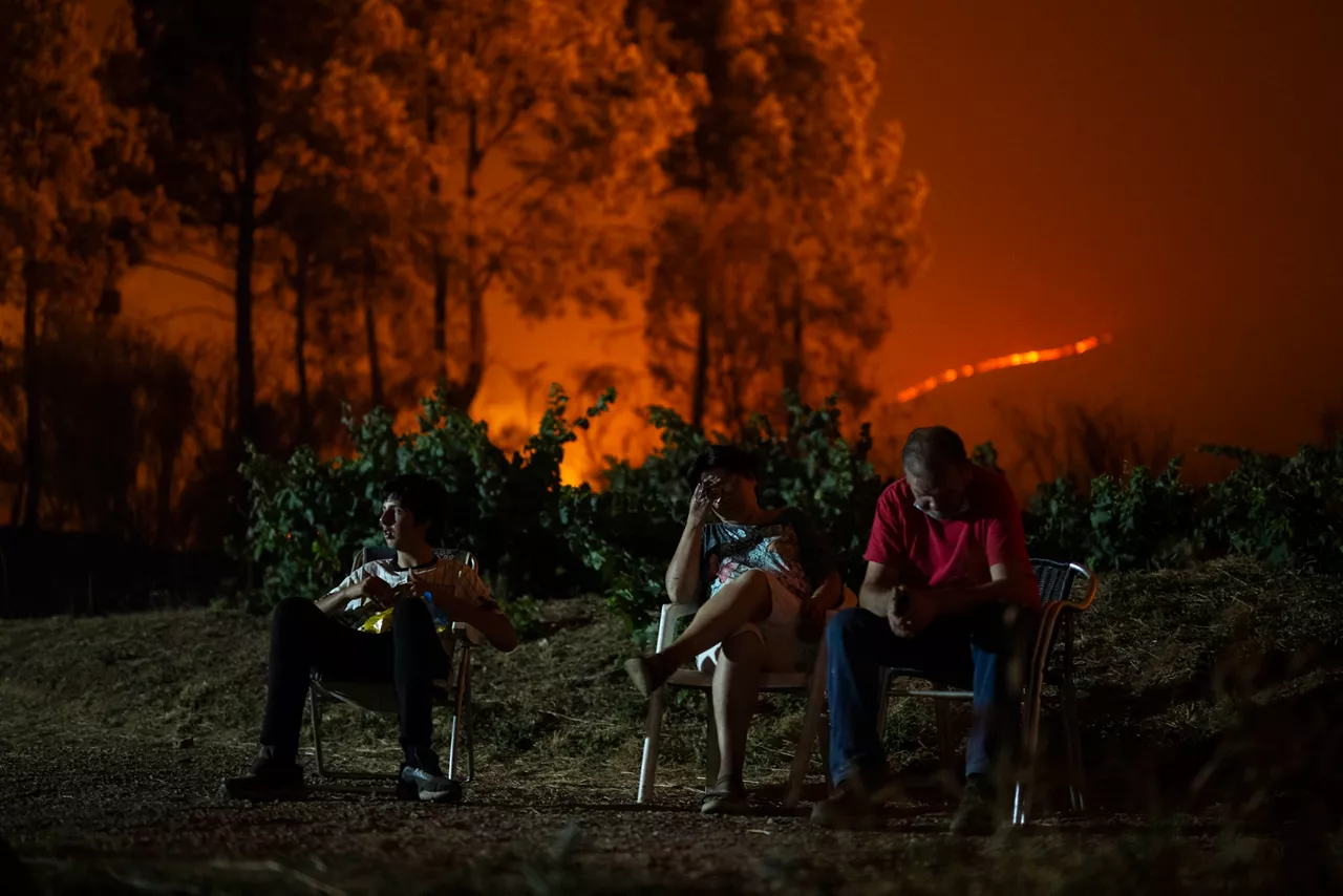 A RÚA (OURENSE), 16/08/2025.- Una familia en el exterior de su vivienda, que ha quedado rodeada por el fuego, en el incendio forestal de A Rúa (Ourense). EFE/ Brais Lorenzo
