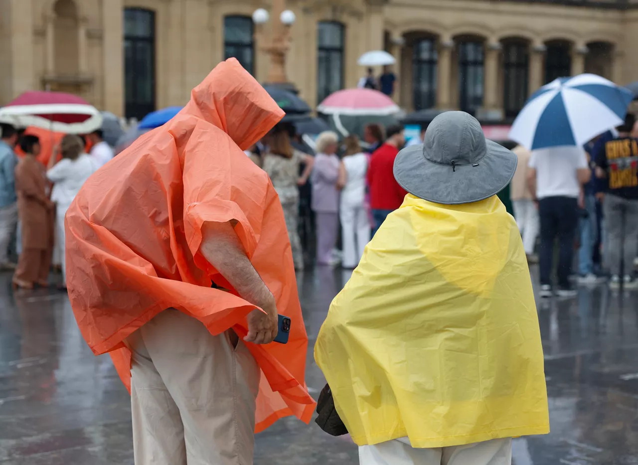 GRAFCAV9515. SAN SEBASTIÁN (ESPAÑA), 02/07/2025.- Unos turistas se protegen de la lluvia con chubasqueros este miércoles San Sebastián. Los cielos en el País Vasco permanecerán muy nubosos con lluvia débil o sirimiri en la vertiente cantábrica, nubosos en la vertiente mediterránea y poco nubosos en el sur de Álava, territorio donde habrá algunas nubes de evolución por la tarde con posibles chubascos tormentosos y ocasionales. EFE/Juan Herrero
