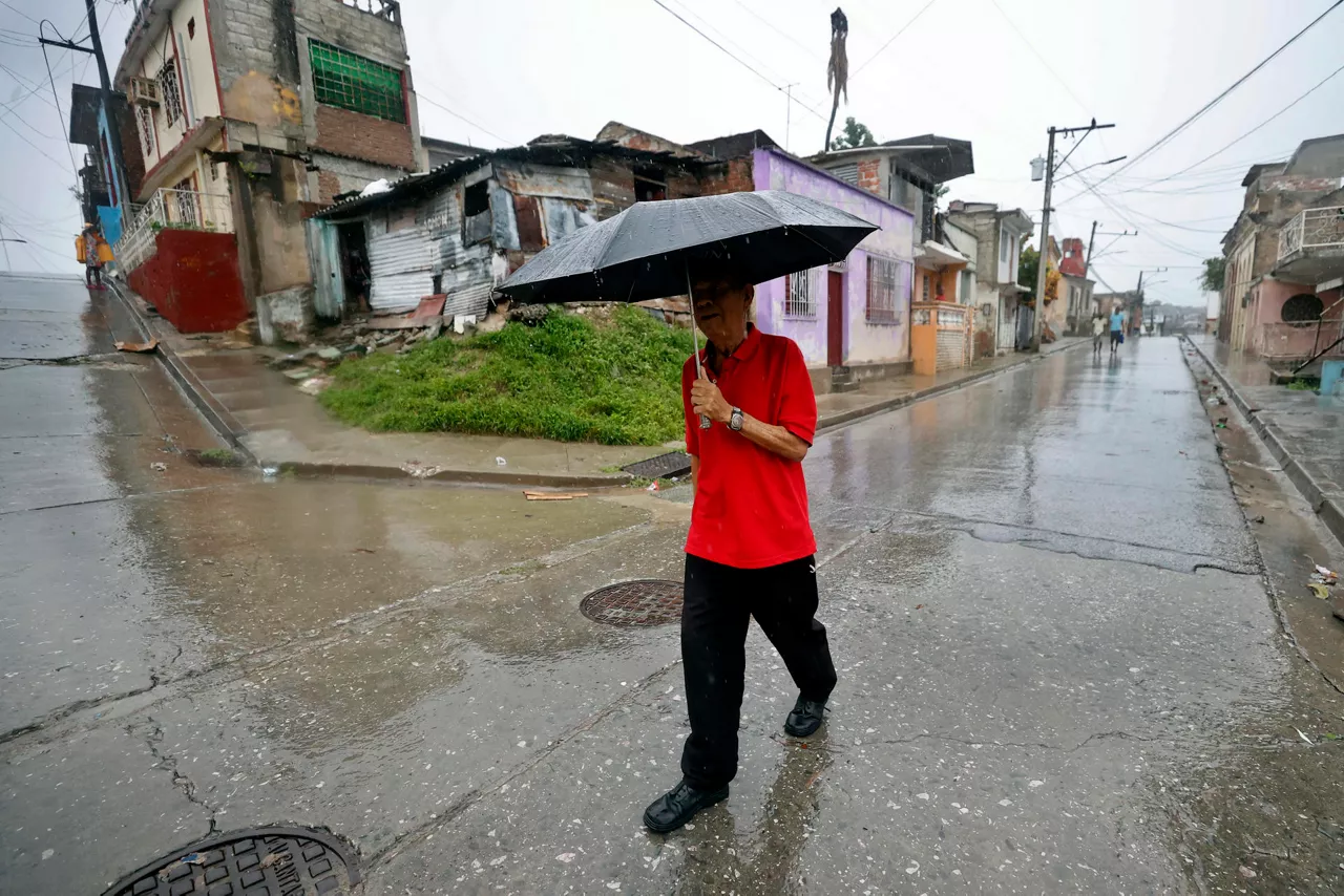 AME2831. SANTIAGO DE CUBA (CUBA), 28/10/2025.- Una persona se protege de la lluvia este martes, en Santiago de Cuba (Cuba). El Instituto de Meteorología (Insmet) de Cuba prevé que Melissa impacte en su extremo oriental como un huracán "extremadamente peligroso", probablemente como un categoría 4 (de 5) en la escala Saffir-Simpson. EFE/ Ernesto Mastrascusa
