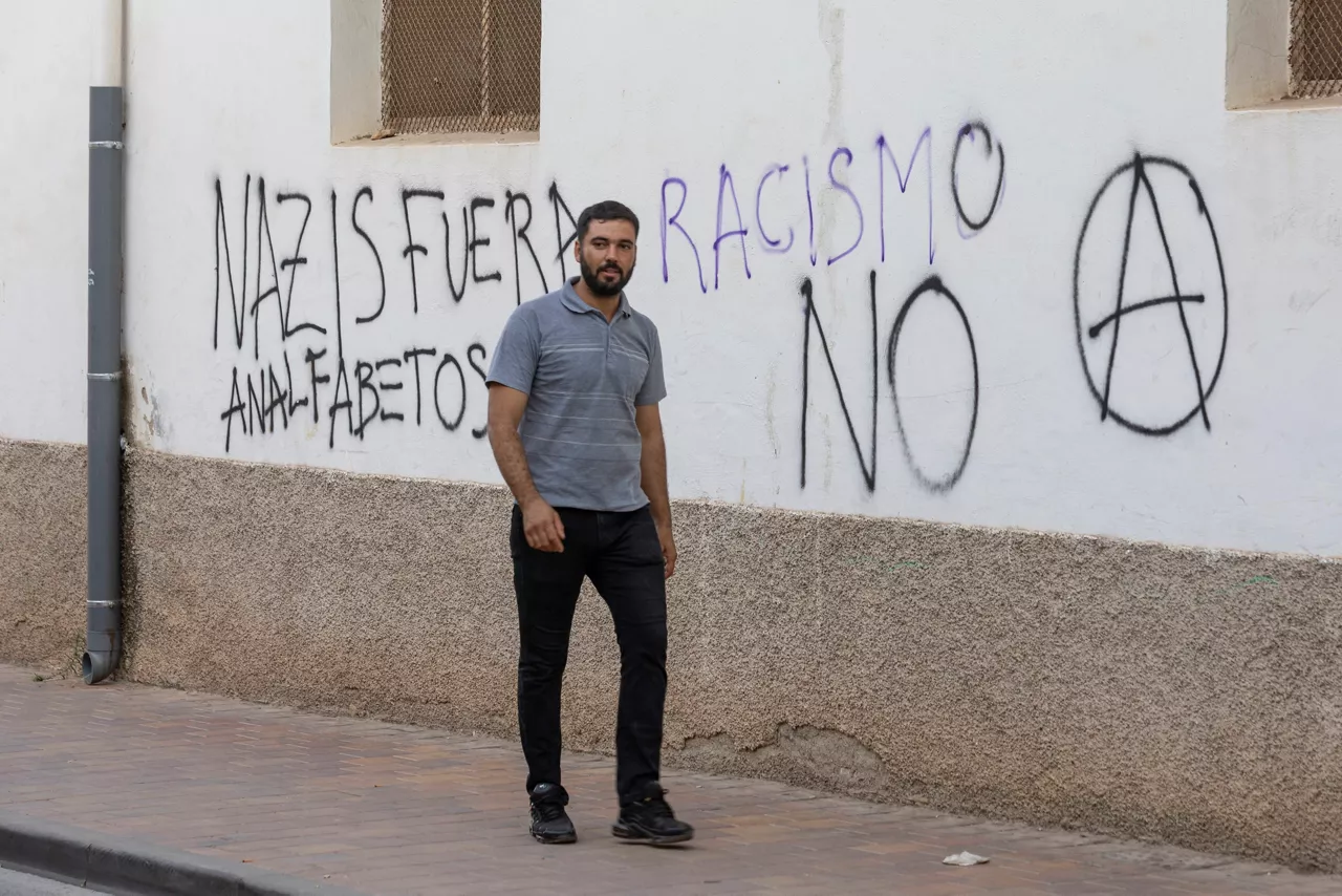 TORRE PACHECO (MURCIA), 16/07/2025.- Un hombre pasa junto a una pintada contra el racismo este miércoles en el barrio de San Antonio de Torre Pacheco (Murcia). La segunda concentración, no autorizada y convocada en redes sociales por grupos ultras, ha tenido nulo seguimiento en una plaza consistorial donde hay absoluta tranquilidad con la excepción de la numerosa presencia de medios de comunicación. EFE/ Marcial Guillen

