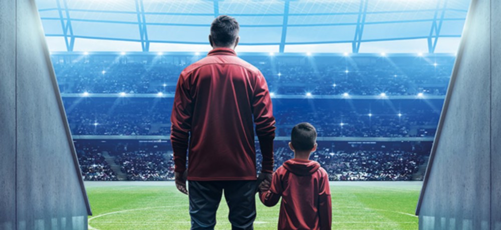 un uomo e un bambino per mano e di spalle all'ingresso del terreno di gioco di un campo da calcio