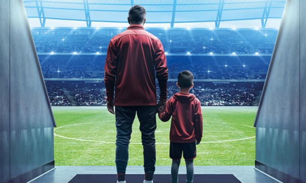 un uomo e un bambino per mano e di spalle all'ingresso del terreno di gioco di un campo da calcio