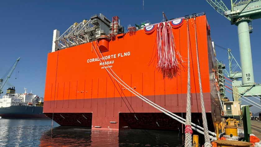 View of the Coral Norte FLNG hull afloat during the launching phase, showing the large orange structure of the unit, mooring lines in the foreground and the shipyard in the background.