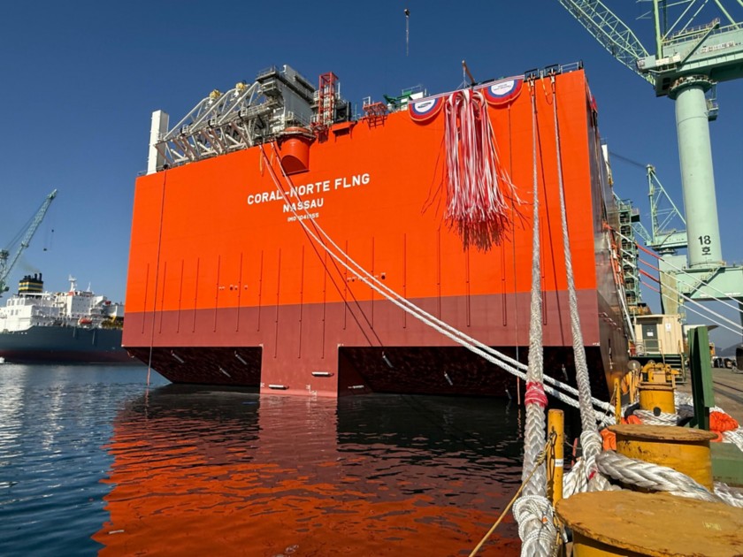 View of the Coral Norte FLNG hull afloat during the launching phase, showing the large orange structure of the unit, mooring lines in the foreground and the shipyard in the background.