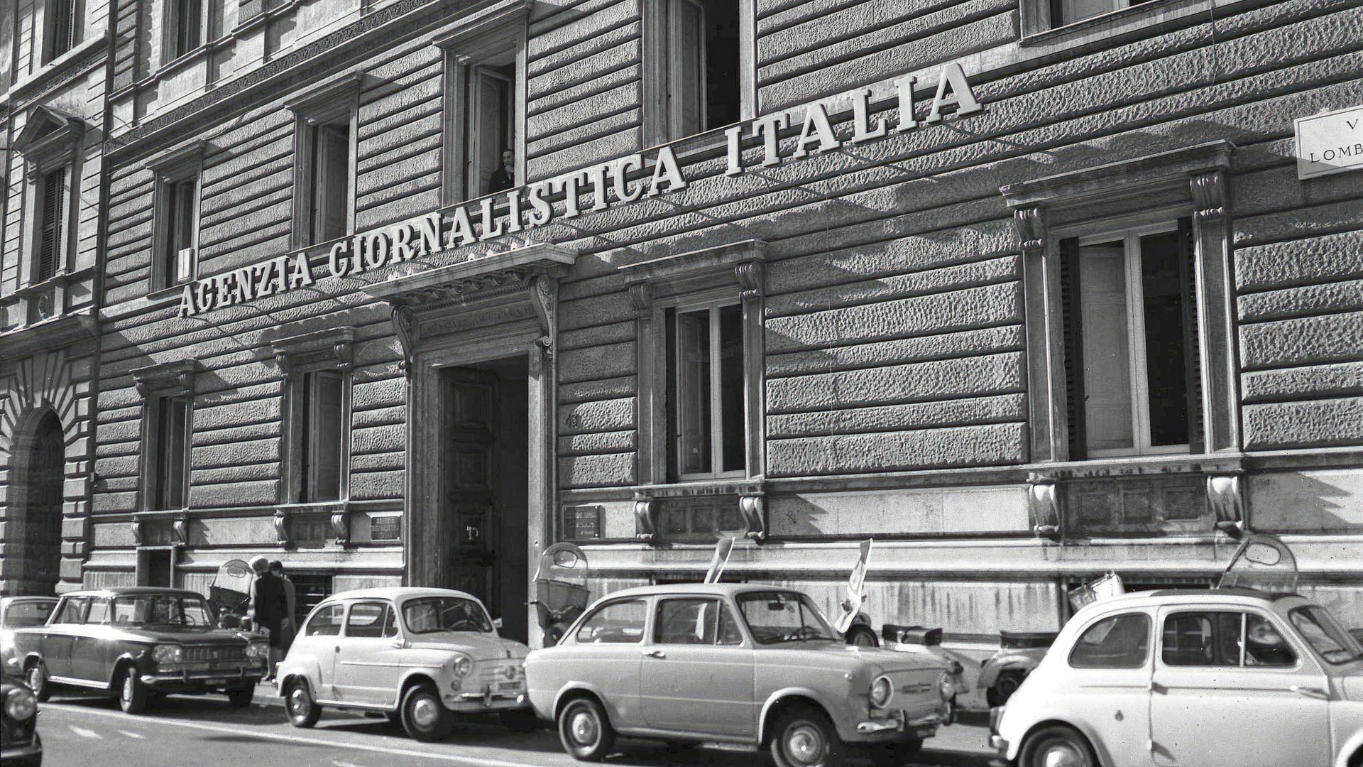 foto storica in bianco e nero di un palazzo con auto parcheggiate e la scritta Agenzia Giornalistica Italia