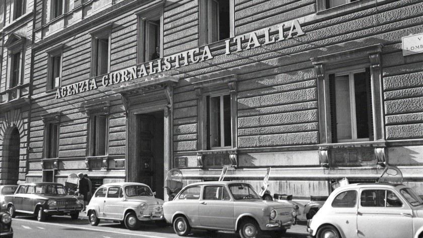 foto storica in bianco e nero di un palazzo con auto parcheggiate e la scritta Agenzia Giornalistica Italia