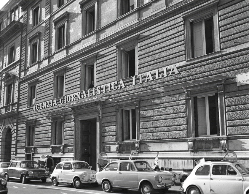 foto storica in bianco e nero di un palazzo con auto parcheggiate e la scritta Agenzia Giornalistica Italia