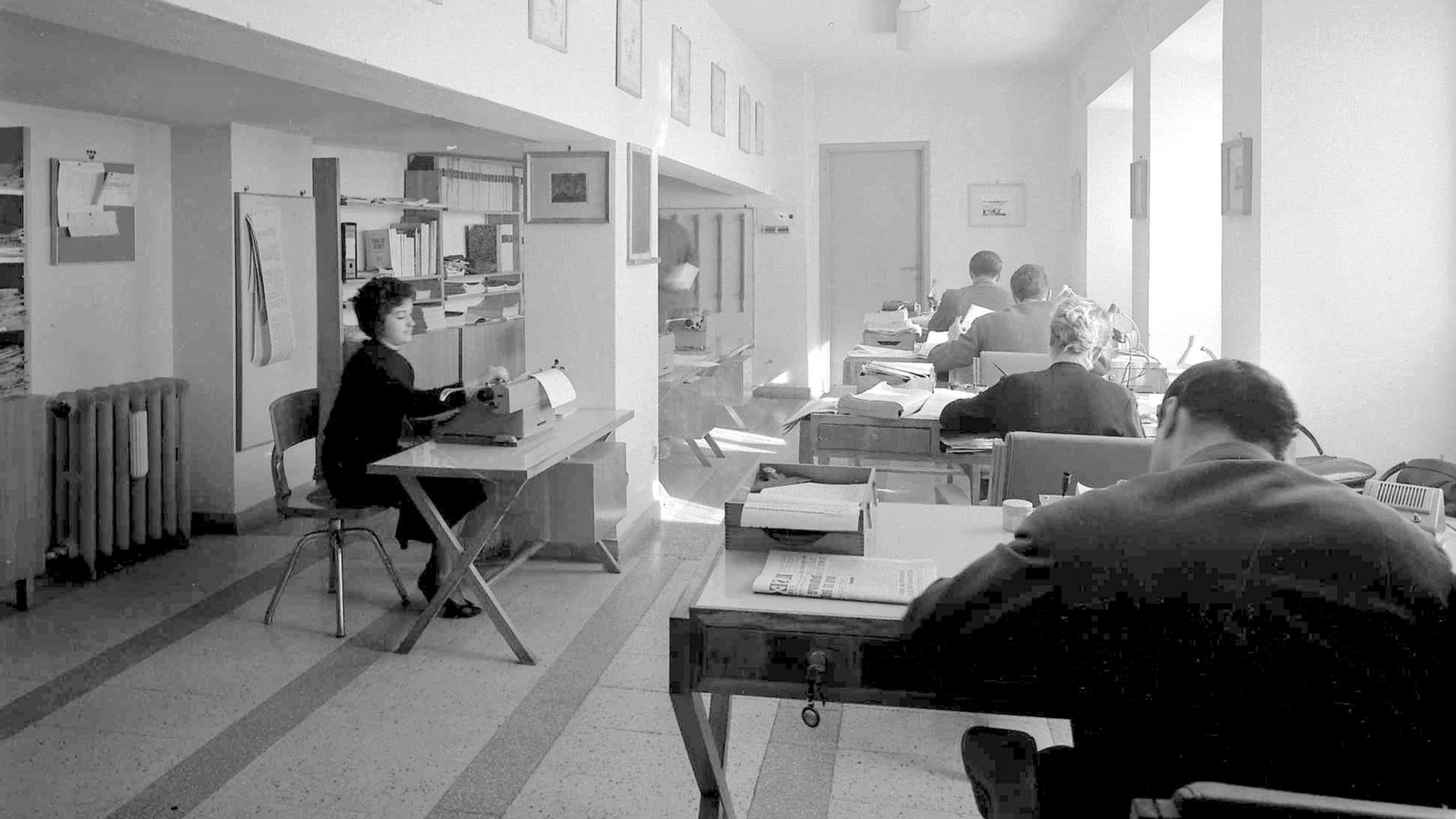 foto storica in bianco e nero con due donne e tre uomini alla scrivania che usano macchine da scrivere