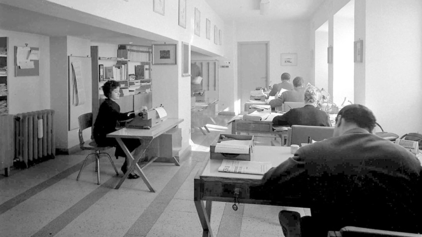 foto storica in bianco e nero con due donne e tre uomini alla scrivania che usano macchine da scrivere