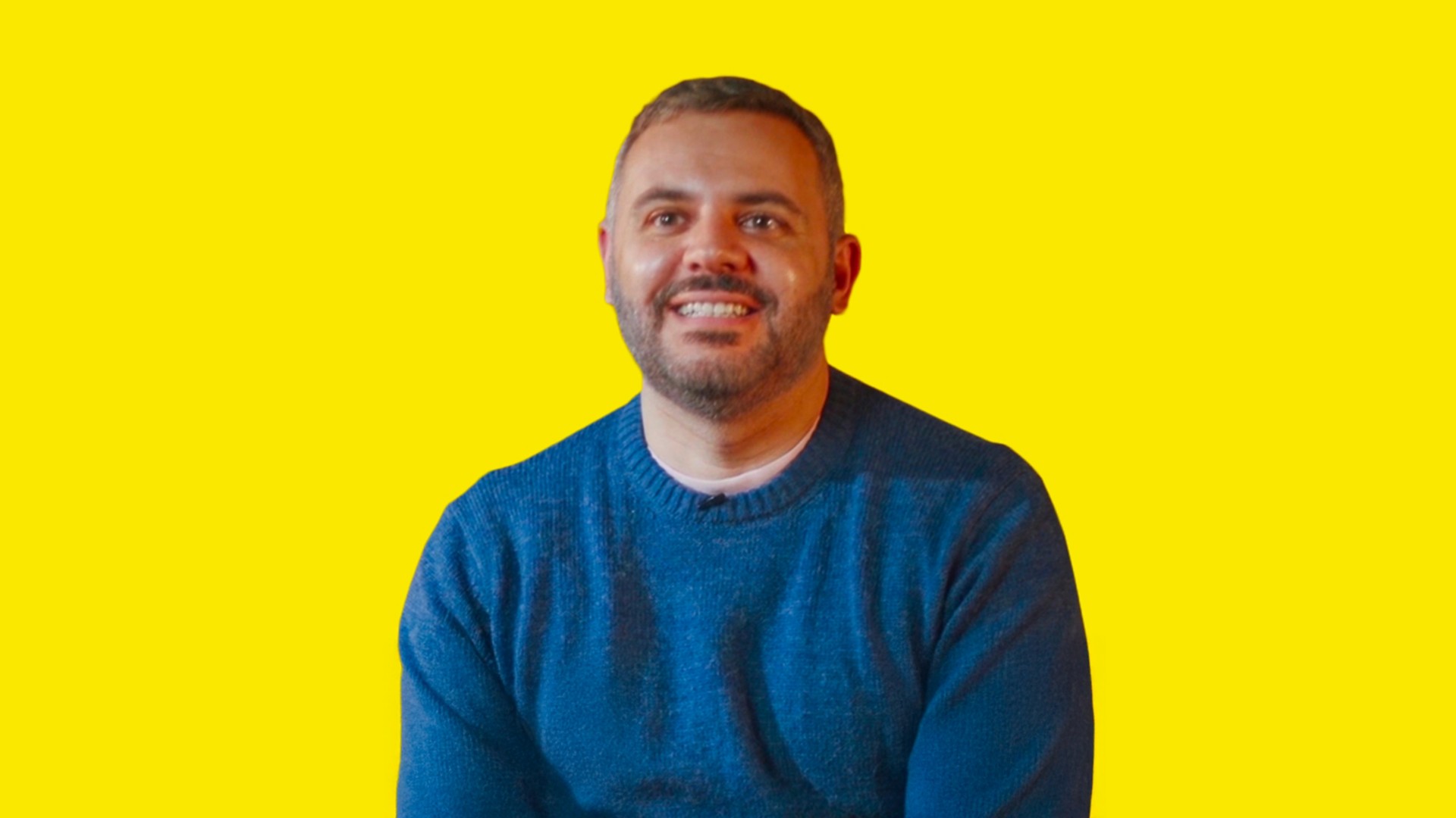 A smiling boy with black hair and a beard and a blue sweater