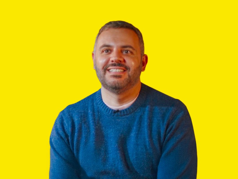 un ragazzo sorridente con i capelli neri e la barba e un golf blu