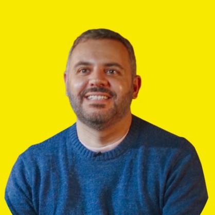 A smiling boy with black hair and a beard and a blue sweater