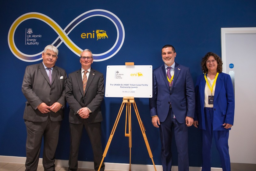 tre uomini e una donna sorridono in posa vicino a un cartello che annuncia la partnership 