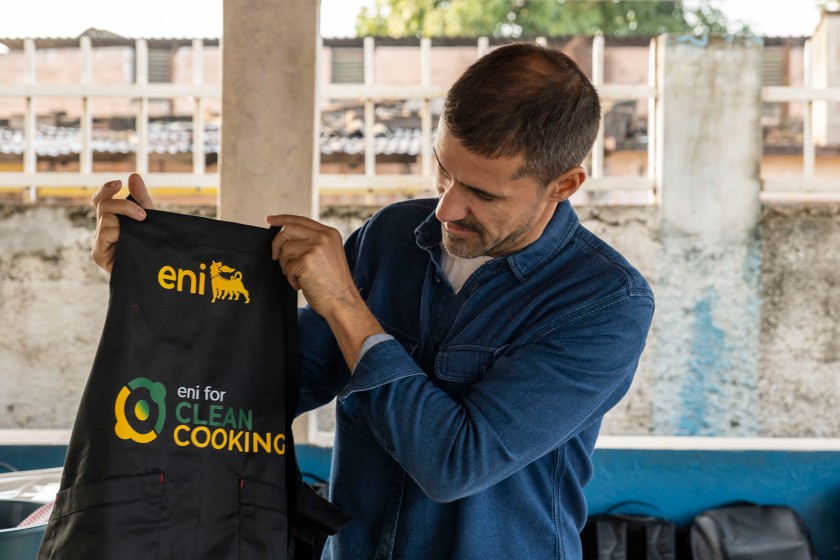 uomo mostra grembiule da cucina nero con logo Eni giallo e scritta Clean Cooking