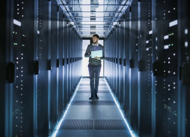 IT technician walking in a data center with a laptop among servers