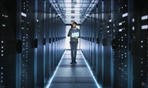 Tecnico informatico cammina in un data center con un laptop tra i server
