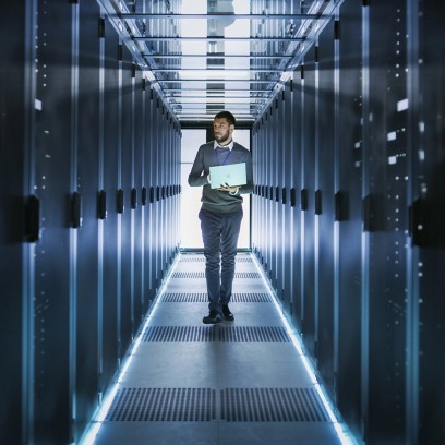 Tecnico informatico cammina in un data center con un laptop tra i server