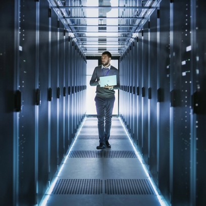 Tecnico informatico cammina in un data center con un laptop tra i server