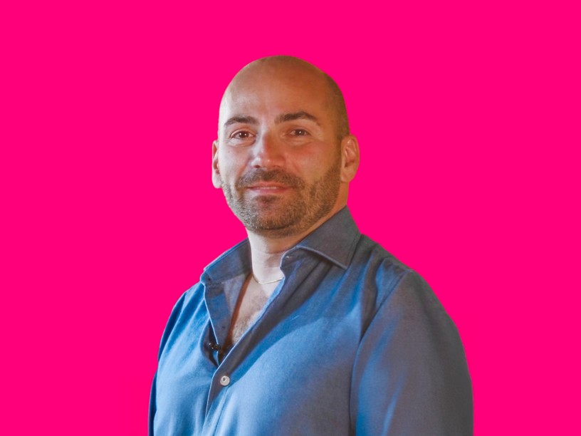 un ragazzo sorridente con i capelli rasati e una camicia blu