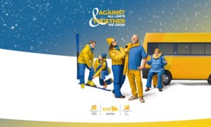 Gruppo di persone in abbigliamento invernale giallo e blu sulla neve, accanto a un furgone giallo, con slogan “Against all limits, together we grow”.