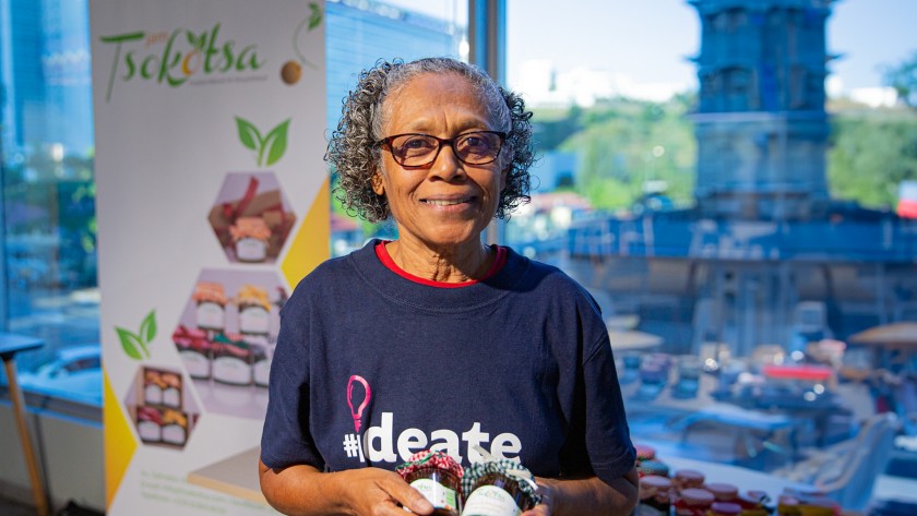 African woman presents her project, holding two jars of jam