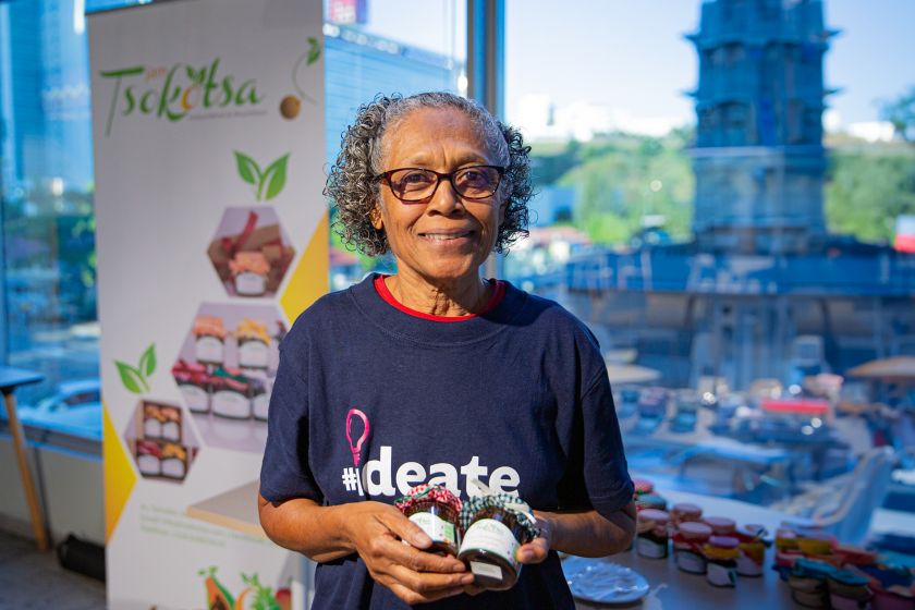 African woman presents her project, holding two jars of jam