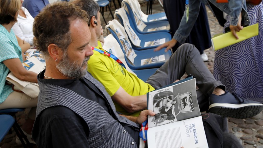 Un uomo seduto del pubblico sfoglia una rivista durante l'evento