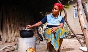African woman cooks a dish with the stove placed on the ground