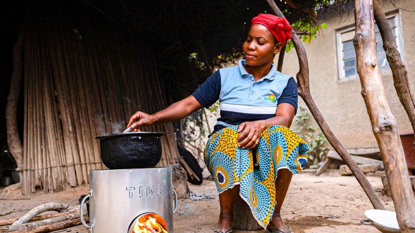 African woman cooks a dish with the stove placed on the ground