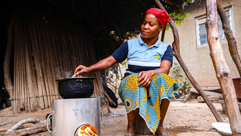 Donna africana  cucina pietanza con il fornello appoggiato a terra