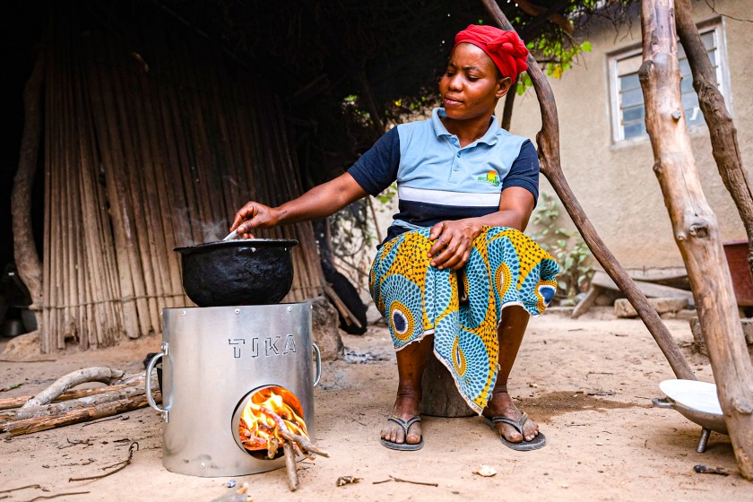 African woman cooks a dish with the stove placed on the ground